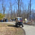 image of carts on a path in a stand of trees with a fire on the right, there a several people in the image as well