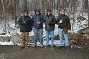 Photo of four clays shooters with snow and trees in the background