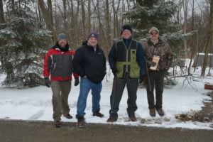 Photo of four clays shooters with trees and snow in background