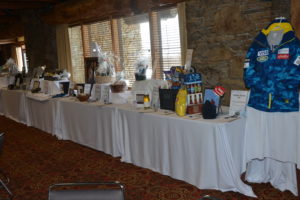 Photo of auction table with white table cloth with prizes on top while having windows behind it