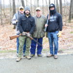 Four men standing together holding shotguns